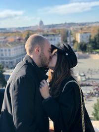 Side view of young couple kissing while standing in city
