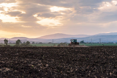 Tractor plowing fields at sunset.