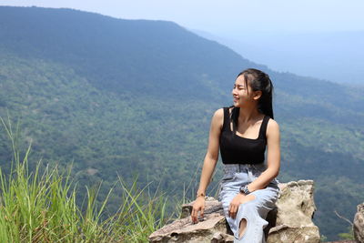 Young woman sitting on mountain against mountains