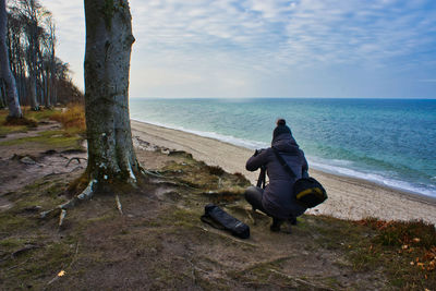 Rear view of woman photographing sea while crouching at beach