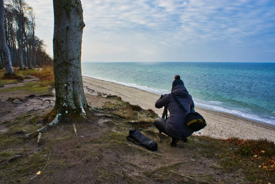 Rear view of woman photographing sea while crouching at beach