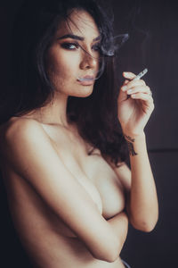 Portrait of sensuous naked woman smoking against black background