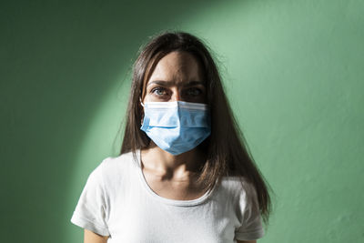 Young woman wearing protective face mask against green wall during covid-19