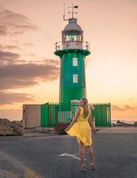 Woman in yellow dress dancing by lighthouse during sunset