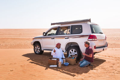 Tourist having a coffee break with his local driver in the desert, wahiba sands, oman