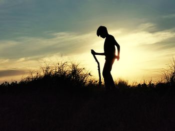 Silhouette boy standing on field against sky during sunset