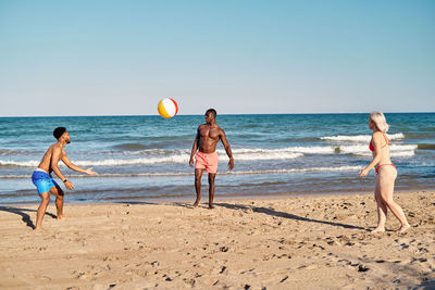 Multiethnic men and women playing beach ball on sandy beach near sea