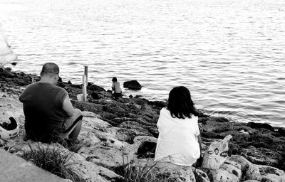 Rear view of couple sitting on rock looking at sea