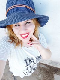 Portrait of smiling young woman wearing hat by wall