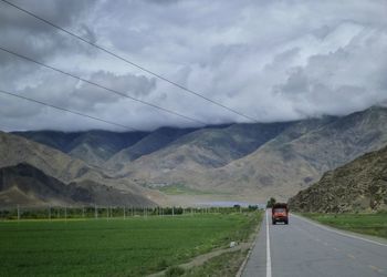 Road amidst field and mountains against sky