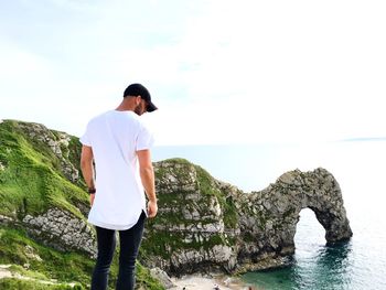 Man standing on rock by sea against sky