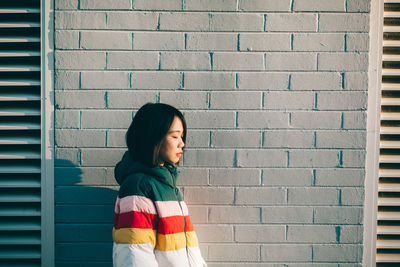 Young woman looking away against brick wall