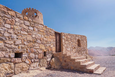 Stone wall of a small medieval arabian fort with wooden door and stone stairs the desert.