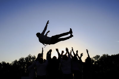 Man jumping over friends against clear sky