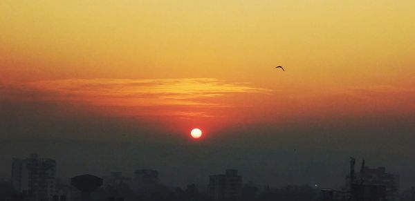 Silhouette birds flying against dramatic sky during sunset