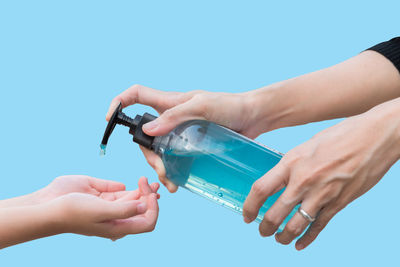 Close-up of hand holding bottle against blue background