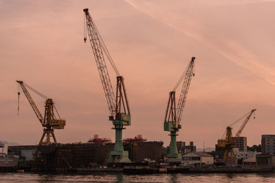 Cranes at  dock against sky during sunset