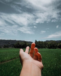 Midsection of person hand on field against sky