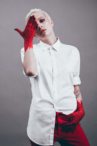 Portrait of young woman with red hands against gray background