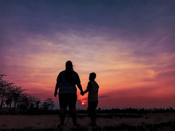 Silhouette woman and son standing against orange sky at sunset