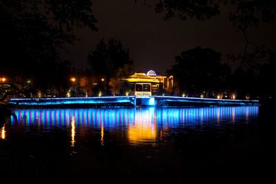 Illuminated building by lake against sky at night