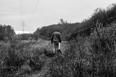 Rear view of mid adult man walking on field against cloudy sky