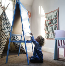 Girl writing on artist's canvas while sitting on rug at home