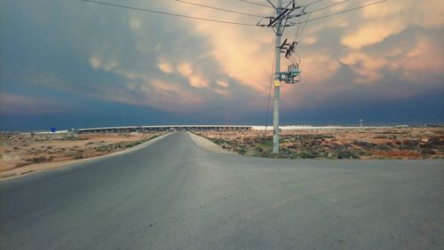 Road amidst electricity pylon against sky