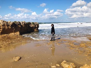 Full length portrait of woman standing at beach against sky