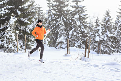 Woman running on snow covered field against trees