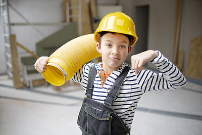 Portrait of boy holding hardhat while standing against wall