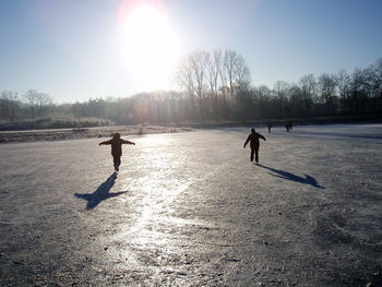 People playing on snowy field against clear sky during winter