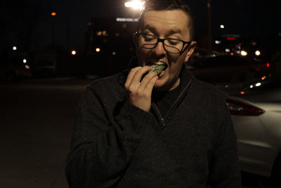 Man eating food while standing on illuminated road in city at night