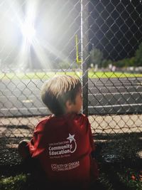 Rear view of boy looking through chainlink fence