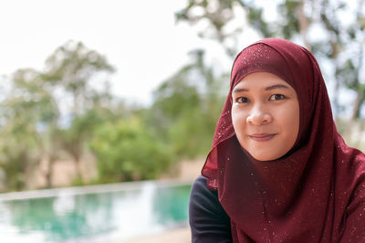 Portrait of woman in red hijab against swimming pool and trees