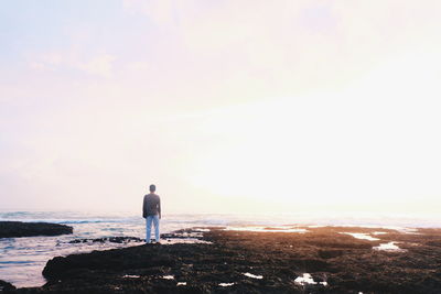 Rear view of man standing on beach against sky