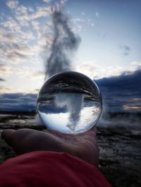 Close-up of hand holding crystal ball against sky