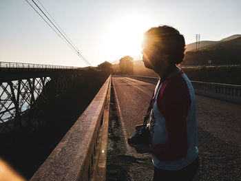 Side view of man standing on bridge against sky during sunset