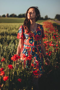 Beautiful young woman standing on field against sky