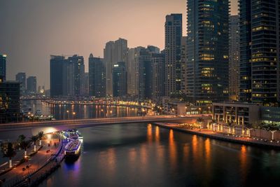 Illuminated buildings by river against sky in city at night