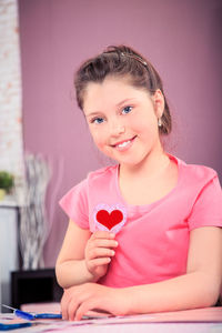 Portrait of smiling girl holding heart shape at home