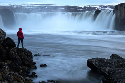 Rear view of woman standing on rock against waterfall 