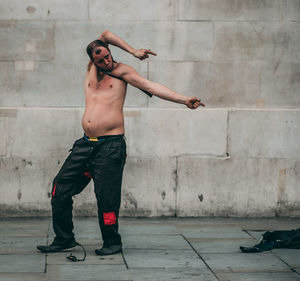 Full length of shirtless man performing while standing against wall