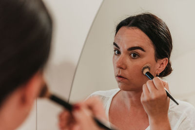 Mirror photo of beautiful young woman putting on make-up