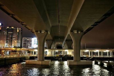 Bridge over river against built structures at night