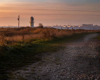 Lighthouse on field against sky during sunset