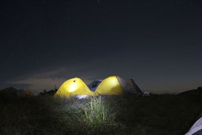 Illuminated tents on grass against sky at night