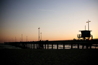 Silhouette pier on beach against clear sky during sunset