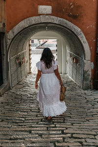Rear view of girl wearing white dress, walking in stone paved alley in picturesque old town