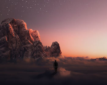 Man on rock against sky during sunset